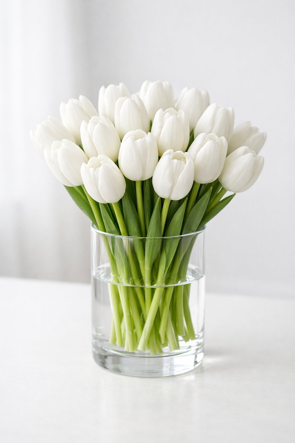 A clear glass vase filled with white tulips arranged on a light-colored table.